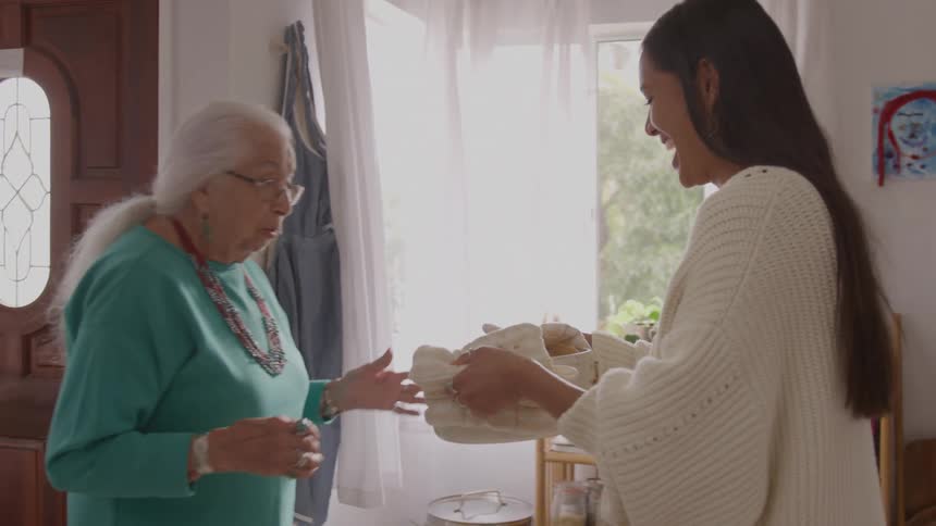 Elderly woman reacts with surprise as the younger woman smiles while holding a basket covered with cloth