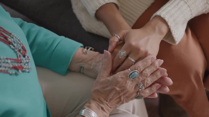 A young woman gently holds the hands of an elderly woman both of them wearing many rings
