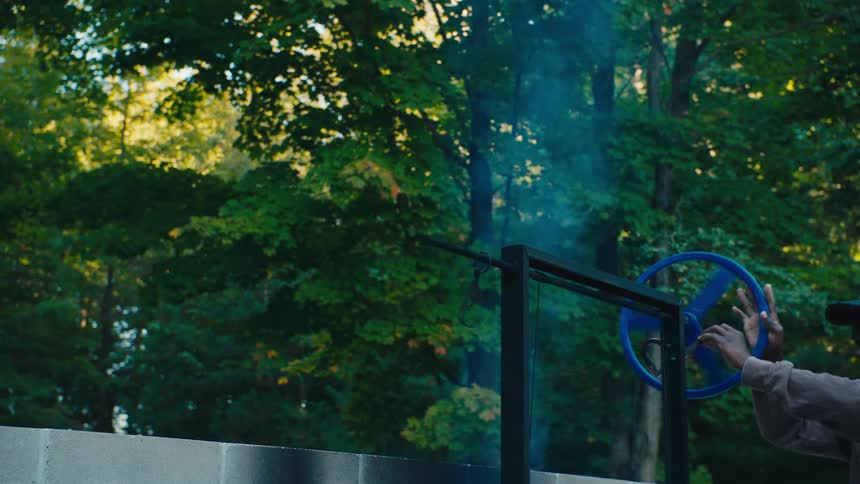 Person turns a blue valve on a large metal structure in a wooded area