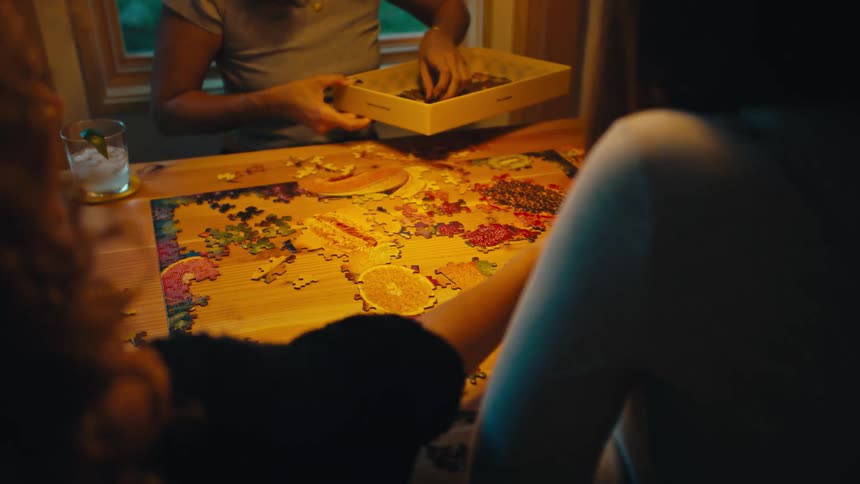 Female friends gathered around dining table building a jigsaw puzzle