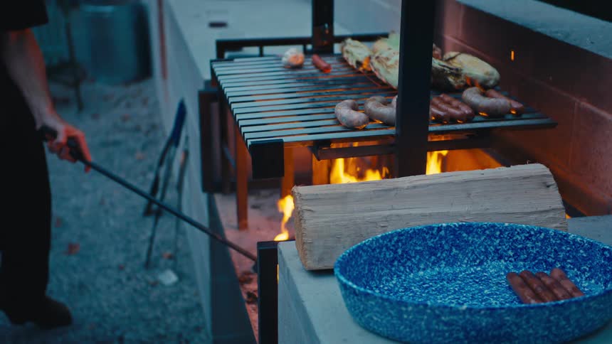 Person adjusting the fire while meats and corn cook on the grill