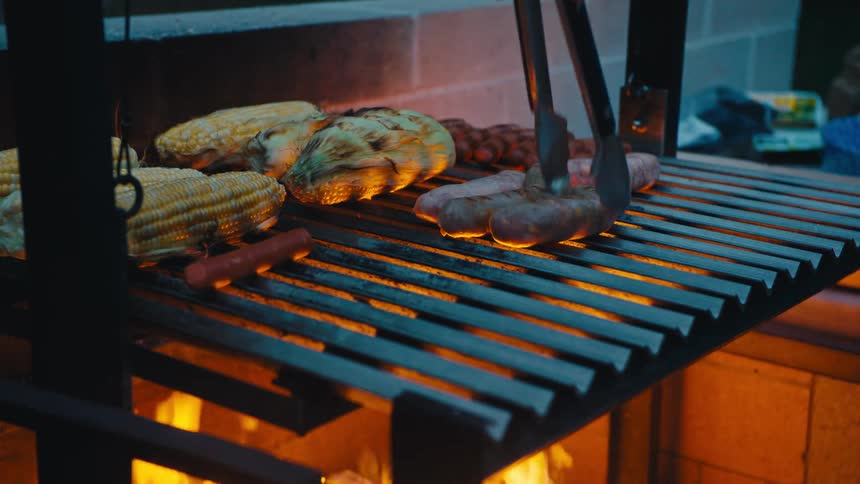 Foods like sausages and corn being grilled over the fire