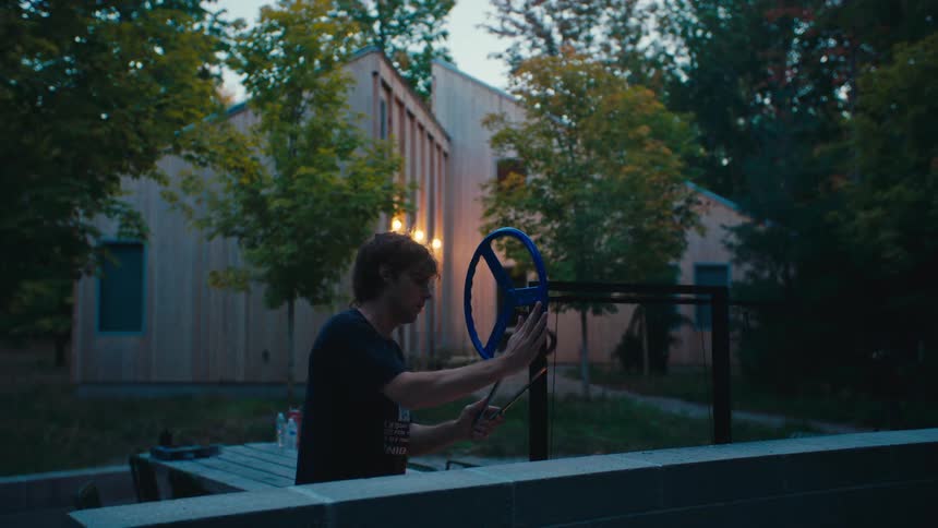 A man grills outside a modern wooden house at dusk