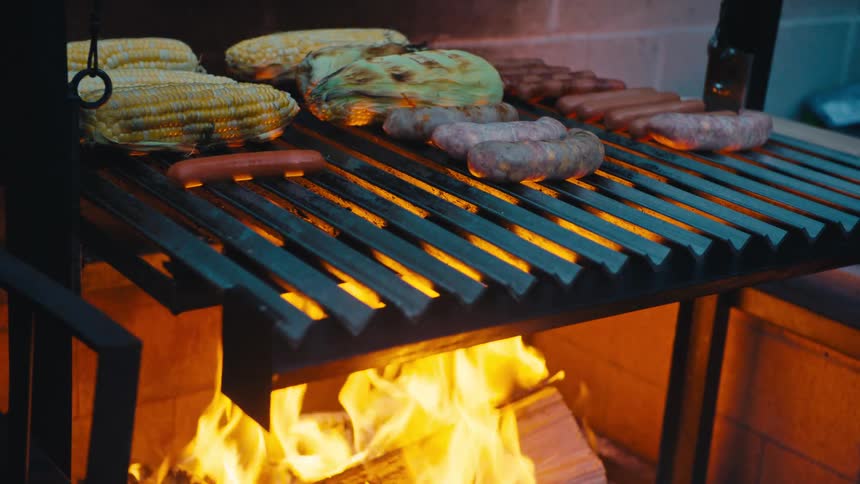 Close up of a person grilling maize and sausages outdoors at night