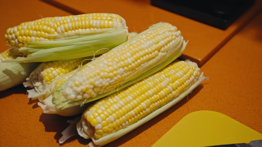 Placing a corn on a pile of corn on an orange countertop