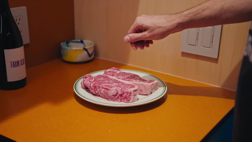 Person adding seasoning to steaks before cooking them
