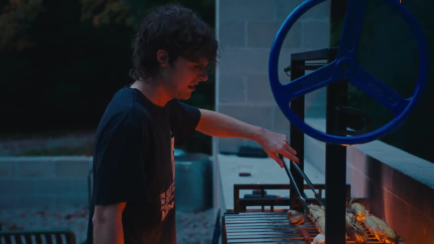 A man grills corn and shrimp on an outdoor barbecue at night