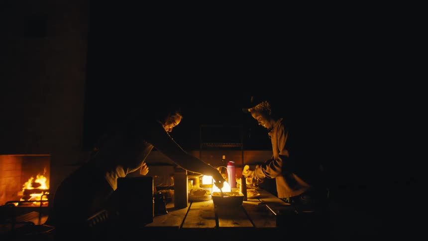 People gathered at an outdoor table lit by a lantern and fire