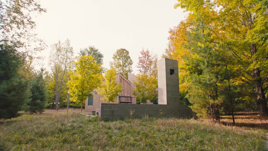 A modern structure with a large concrete chimney sits in a field surrounded by fall trees displaying bright yellow and orange leaves under a bright clear sky
