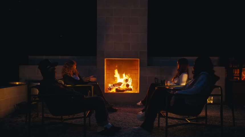 Group of people chatting around an outdoor fireplace at night