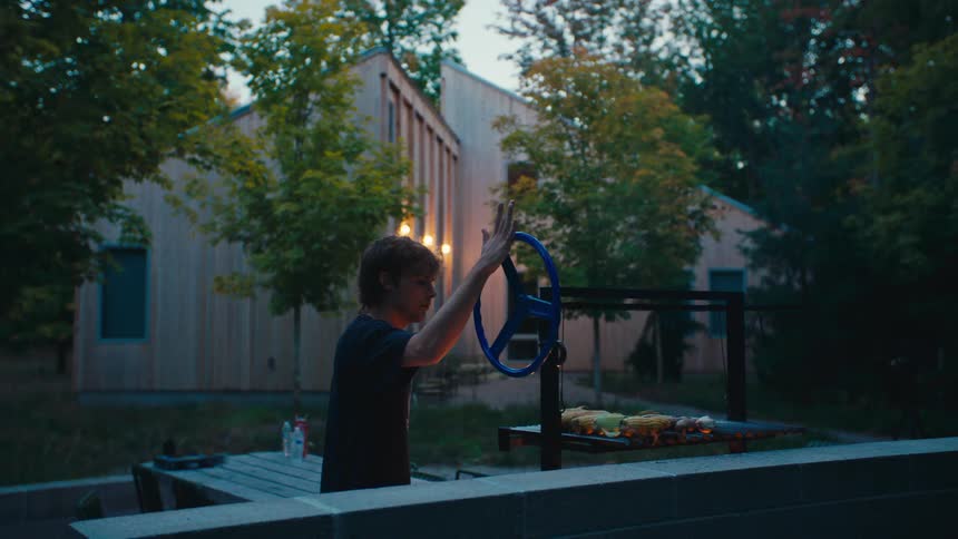 The man turns a wheel on the barbecue to raise the grilling vegetables up