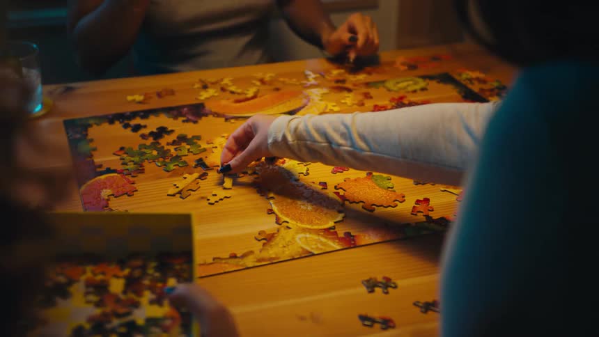 Hands collaborate to assemble a colorful puzzle on a wooden table