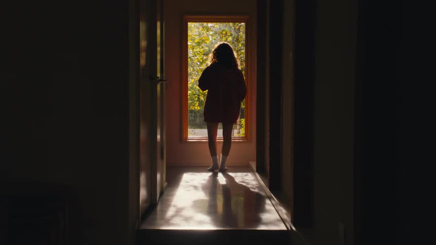 Person looks outside through a sunlit window at dusk