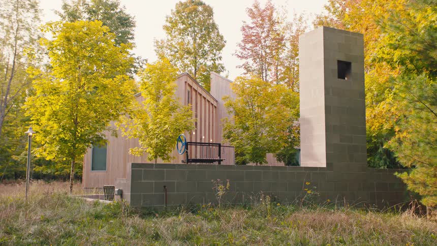The video displays an architecturally distinct home nestled in a forest surrounded by trees with bright yellow and orange foliage suggesting autumn the house features a modern multilevel design with both wood siding and a prominent tall conc