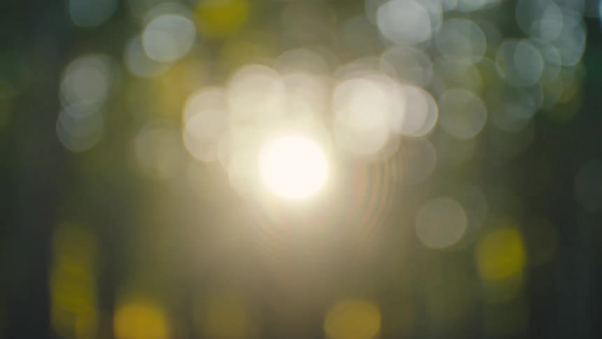 Out of focus shimmering bokeh lights and a bright lens flare against a dark moody background