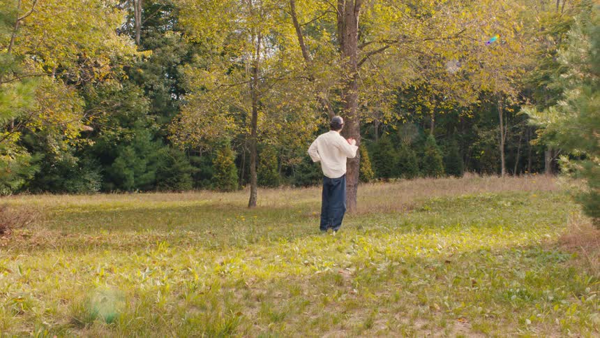Man standing in a wooded field talks on the phone under soft daylight