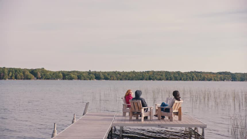 Three friends relax and enjoy coffee on a dock by the lake
