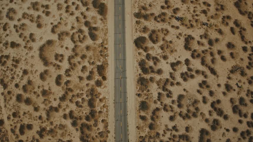 A freeway stretches through a landscape of dry grasses and desert sand on a sunny day shimmering under the heat and clear blue sky
