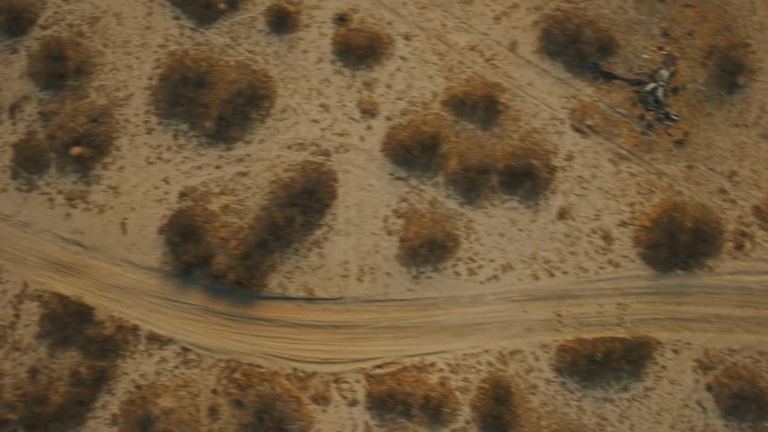 Dirt road cuts through arid landscape with scattered shrubs showing tire tracks across the sandy terrain