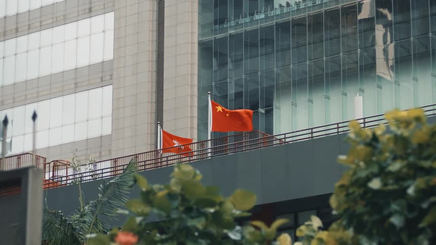 Red flags wave in front of a modern building with a glass facade