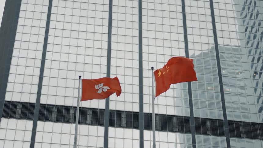 The flags of the hong kong special administrative region sar and the peoples republic of china fly side by side in front of a skyscraper building at midday