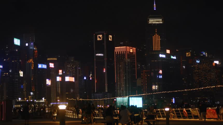 City skyline lit up at night with people gathered by the waterfront observing the buildings