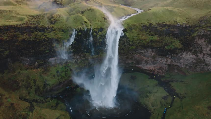 Waterfall next to a cliff and a crowd of people wacthing it outdoors during day time