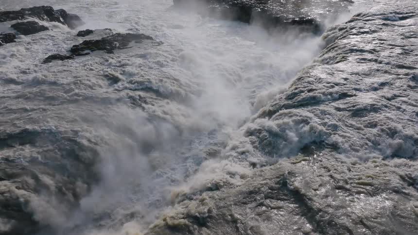 Turbulent current crashes against the rocks raising mist above the flowing river
