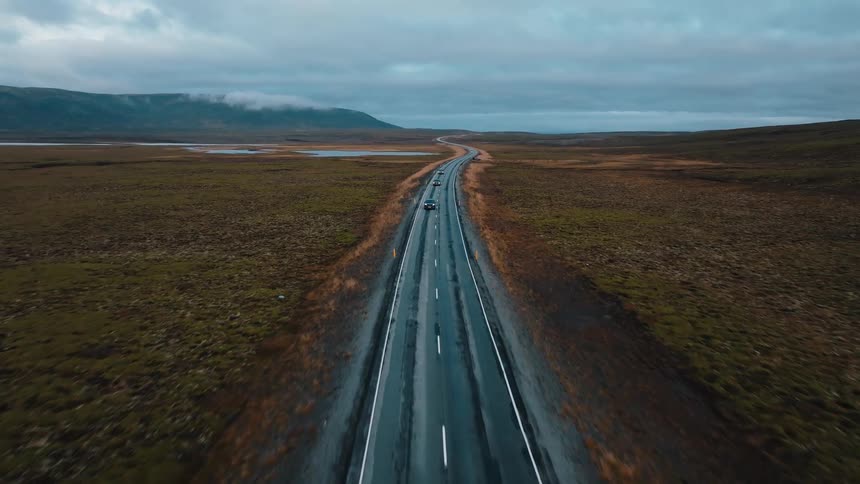 Cars driving on a road surrounded by a natural landscape with bodies of water and mountains outdoors during day time