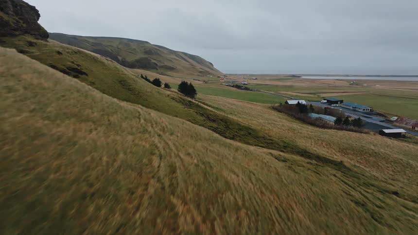 Aerial view of a grassy hillside and plain with a road and buildings below