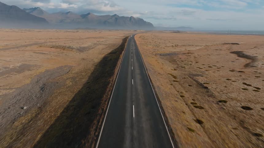 Straight road crossing an arid plain with mountains in the background