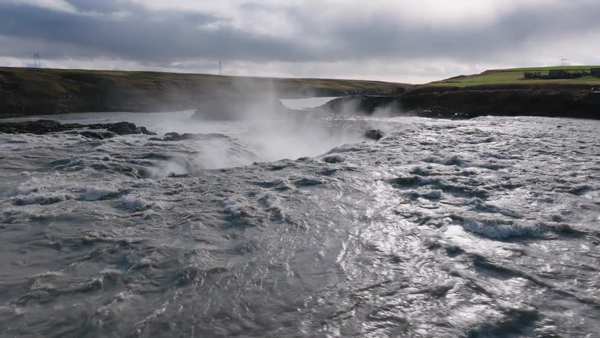 Strong current plunges into a waterfall under cloudy skies and strong winds