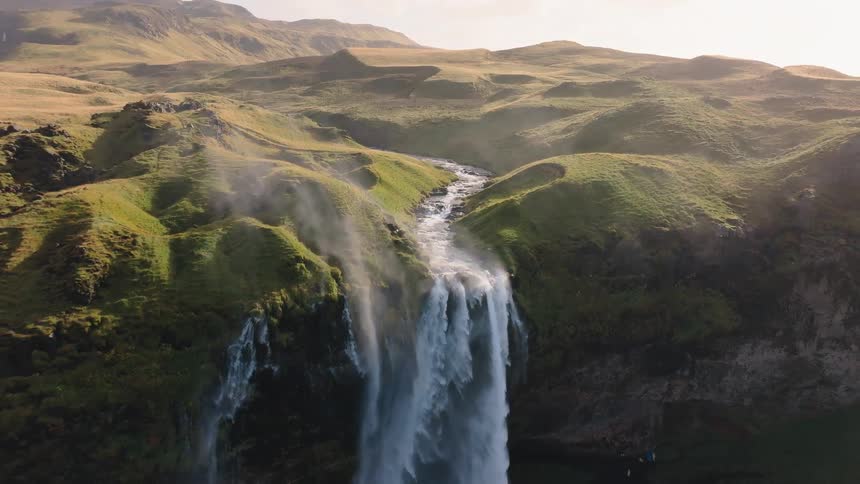 Stream winds between green hills under the soft light of sunset