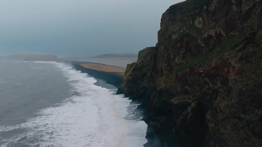 Aerial view of a waves breaking on a beach near rocky cliffs