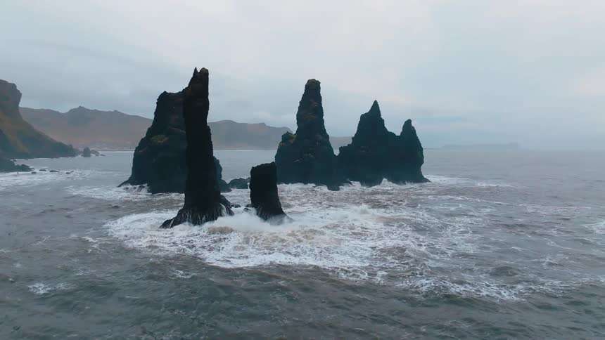 Dark rock formations rise from the sea under a cloudy sky near the coast