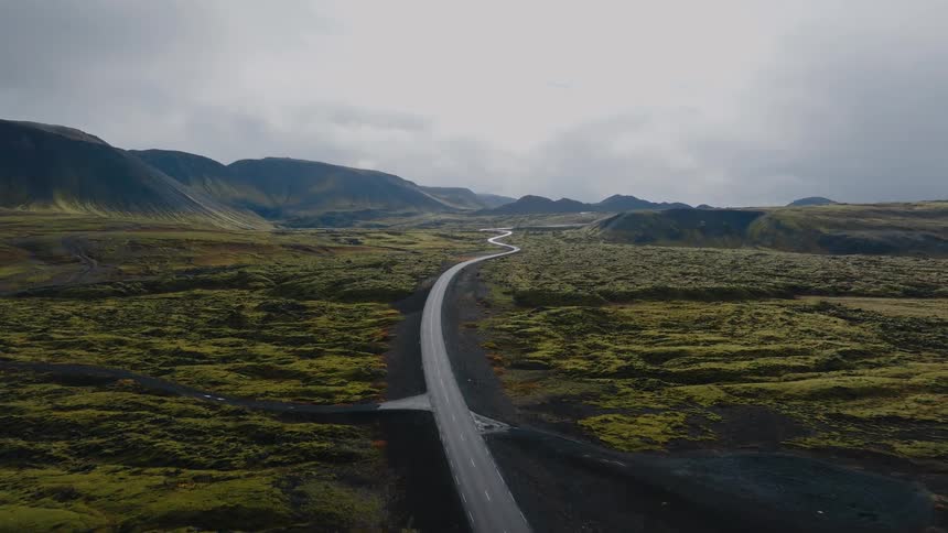 Winding road stretches through a vast mountainous landscape covered with green vegetation