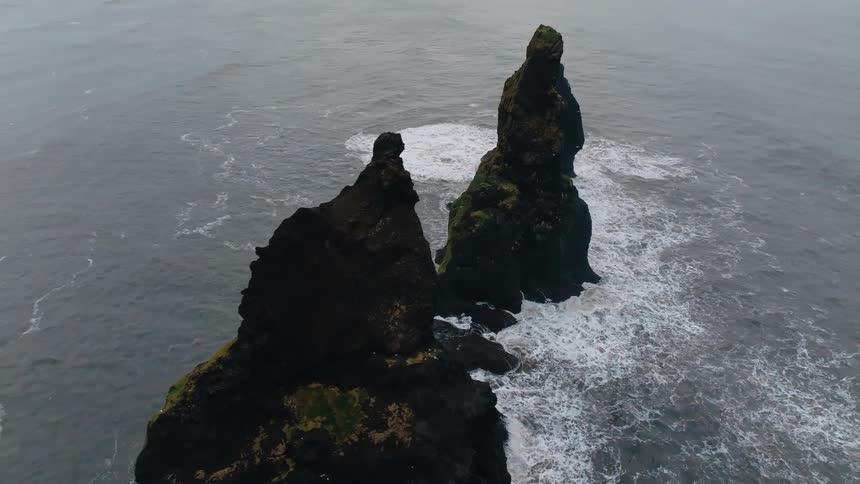 Dark rock formations rise from the sea as waves crash at their base