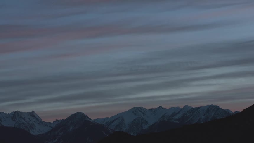 Snowy mountain range under a bluish and pinkish sky at dusk