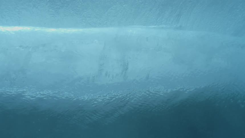 Underwater wave captured in motion with bubbles and bluish foam