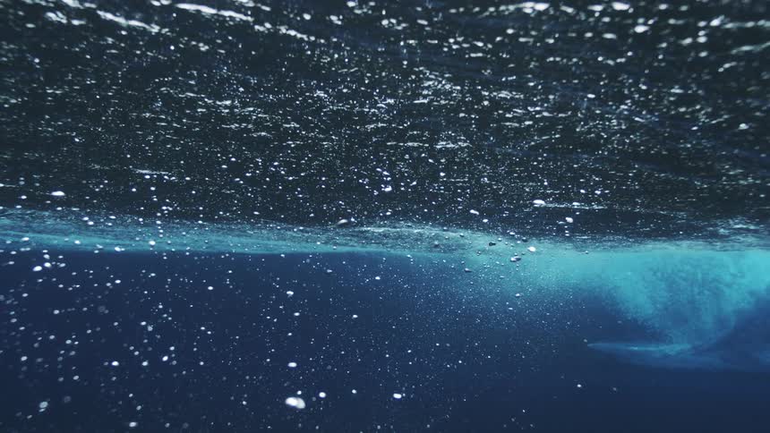 Waves seen from underwater reveal bubbles and bluish reflections in motion