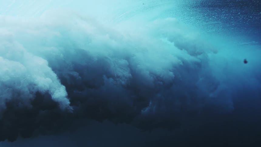 Wave seen underwater forming a turbulent mass of blue foam