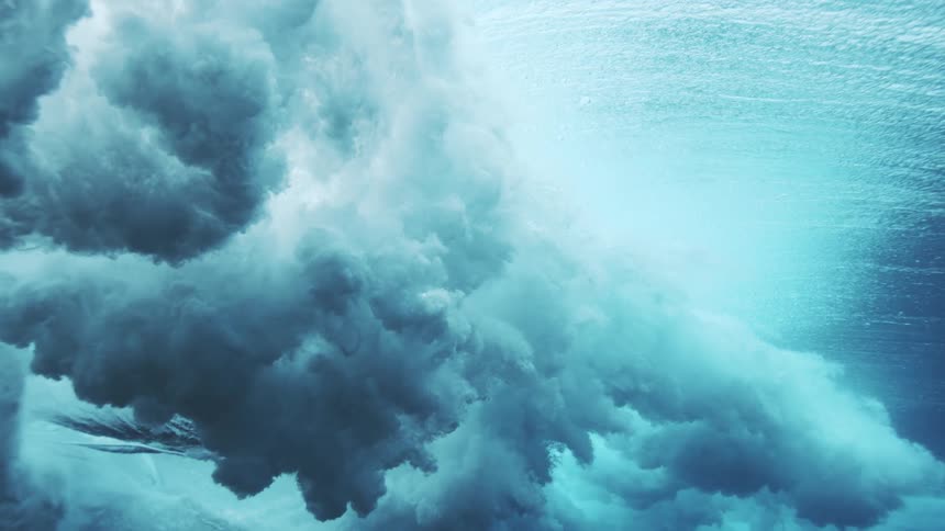 Violent ocean waves crash and form in the open sea at midday churning the water into a foamy turbulent body beneath the bright sun