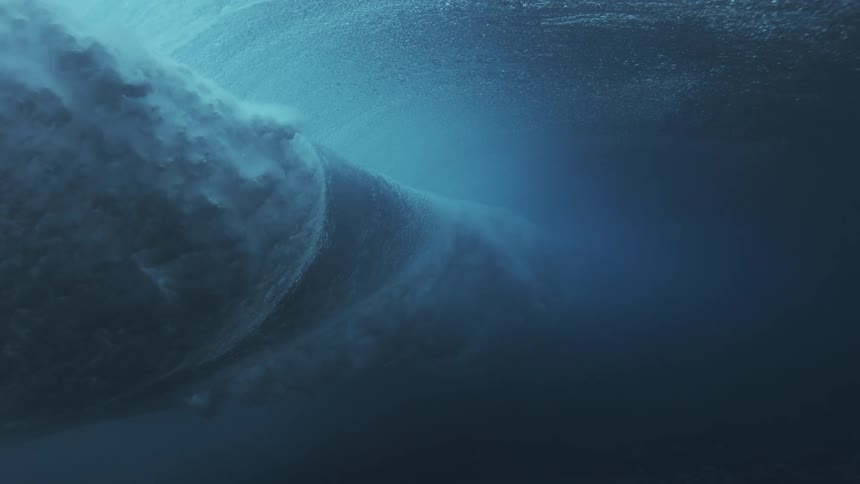 A surfer rides a crashing wave in the ocean at midday carving through the turbulent water as sunlight glints off the foamy crests