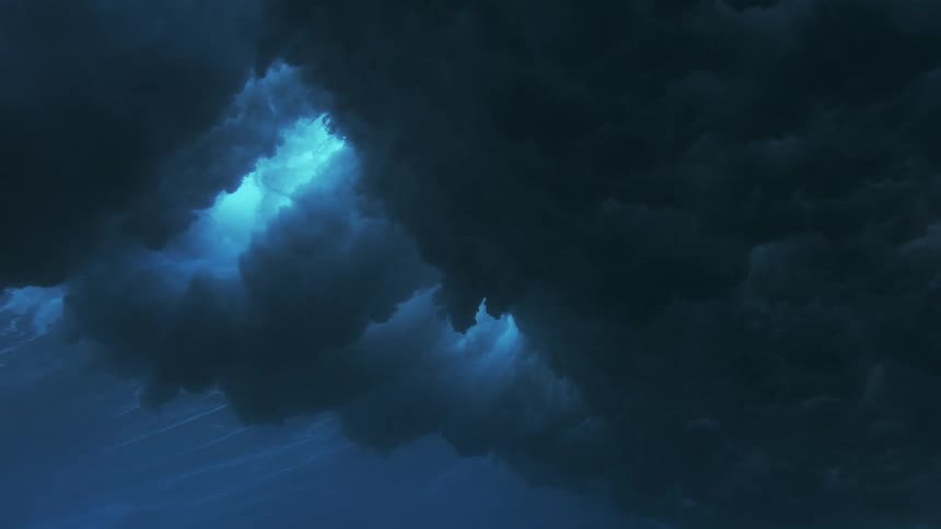 An underwater view captures the dramatic collapse of a large ocean wave filling the deep blue water with massive clouds of white foam and sparkling air bubbles