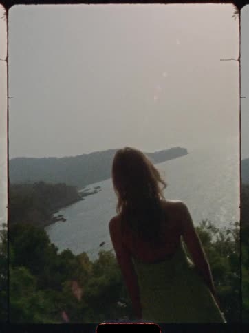 The woman stands on a mountain overseeing the shore