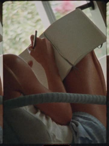 Close up of a young woman drawing in a book while sitting indoors by the window during daytime