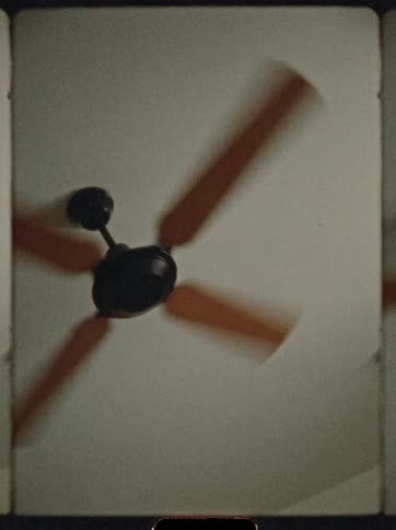 A blurry close view from below shows a black ceiling fan with reddish brown blades spinning rapidly against a plain white ceiling