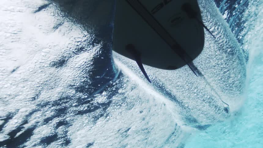Surfboard slices through the underwater surface leaving a trail of bubbles and light