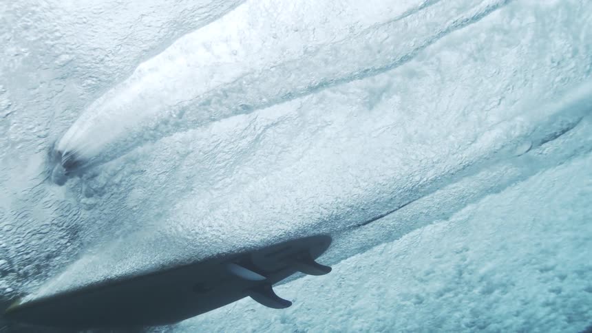 Surfer seen from underwater while riding through the inside of the wave