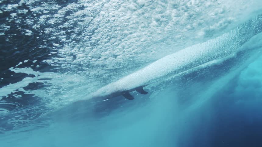 Human silhouette moves through forming wave beneath the surface with filtered light highlighting water motion